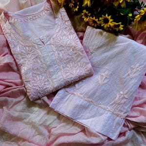 May include: A light pink cotton tunic and matching trousers set featuring intricate tonal floral embroidery. The tunic has a round neckline with a small centre slit, and the trousers feature embroidered floral motifs along the lower hem.