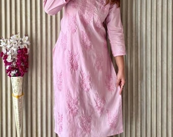 May include: A light pink embroidered kurta and matching pants set. The outfit features intricate floral embroidery and a relaxed fit. The ensemble is paired with cream-colored flats. The background has a vertical striped pattern.
