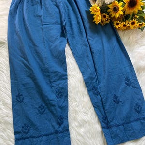 May include: Blue wide-leg trousers featuring an elastic waistband with a white drawstring and tonal floral embroidery scattered across the lower legs, finished with a horizontal stitched hem detail near the bottom of each trouser leg.