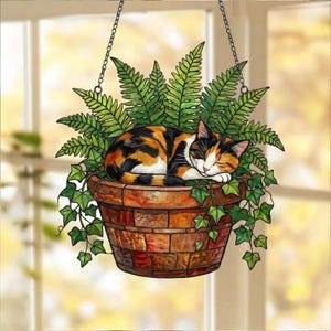 May include: A hanging planter with a sleeping calico cat nestled among green ferns and ivy. The planter is a mosaic of brown and orange tiles, suspended by a chain. The cat has orange, black, and white fur.