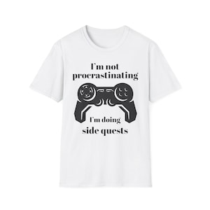 Könnte beinhalten: Weißes T-Shirt mit schwarzer Grafik eines Videospiel-Controllers und dem Text "I'm not procrastinating, I'm doing side quests." Ein lässiges Kleidungsstück.