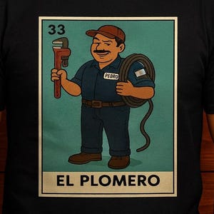 May include: Black t-shirt with a cartoon image of a plumber holding a wrench and a coil of pipe. The illustration includes the number 33 and the words "EL PLOMERO". The man in the image is smiling.