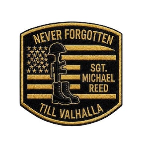 May include: A black and gold patch with the words "NEVER FORGOTTEN" and "TILL VALHALLA". The patch features a helmet, rifle, and boots, with the name "SGT. MICHAEL REED" and a depiction of the American flag.