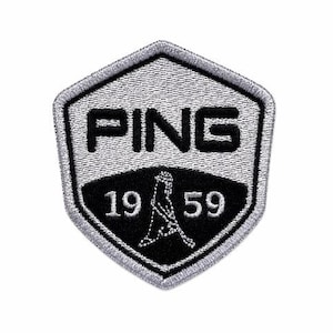 May include: A gray and black embroidered patch with the word "PING" at the top. Below the word "PING" is the year "1959" and a golf club design. The patch is in a shield shape.
