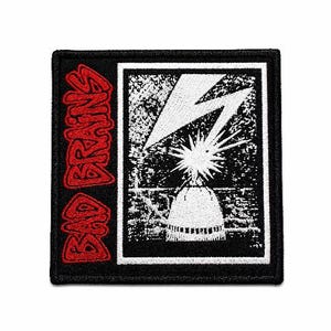 May include: A black and white patch featuring a lightning bolt over a dome, with the text "BAD BRAINS" in red on the left side. The patch has a black border and is likely for clothing or accessories.