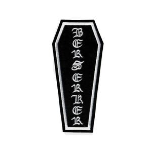 May include: Black coffin-shaped patch with white border and text. The vertical text reads "BERSERKER" in a gothic font. The patch is likely for clothing or accessories.