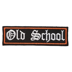 Puede incluir: Un parche rectangular bordado con fondo negro y el texto blanco Old School en fuente gótica. El parche está bordeado por una fina línea naranja y un borde exterior negro, creando un contraste marcado para el diseño bordado.