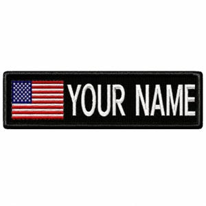 May include: A rectangular black embroidered patch featuring a small United States flag on the left side and the white text YOUR NAME in a bold, sans-serif font on the right side, all enclosed within a thick black stitched border.