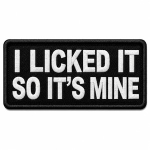 May include: A rectangular black embroidered patch with a thick black border. The patch features the white embroidered text "I LICKED IT SO IT'S MINE" in a bold, sans-serif font, centered across two lines against the black fabric background.