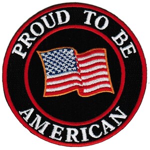 May include: A circular embroidered patch featuring a black background with a red border. The text PROUD TO BE AMERICAN is stitched in white capital letters along the edge. In the center, a waving American flag is depicted with red and white stripes.