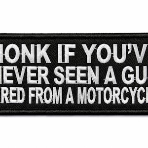 Puede incluir: Un parche rectangular negro bordado con un borde blanco. El texto HONK IF YOU'VE NEVER SEEN A GUN FIRED FROM A MOTORCYCLE está bordado en letras mayúsculas blancas en el centro del parche con una fuente sans-serif en negrita.