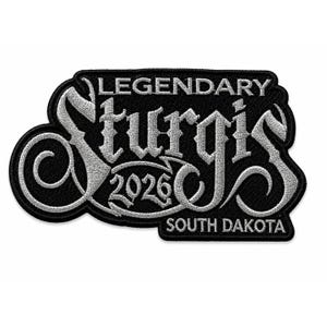 Puede incluir: Un parche bordado negro con el texto plateado LEGENDARY STURGIS 2026 SOUTH DAKOTA. El diseño utiliza una fuente gótica estilizada con una S mayúscula prominente y en espiral, junto a un borde negro, creando un aspecto de alto contraste.