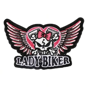 May include: Embroidered patch with a skull wearing a pink bow, pistons, and wings. The design uses pink, black, and white, with the words "LADY BIKER" in a bold font.