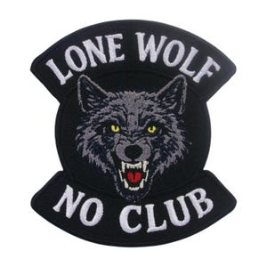 May include: A black embroidered patch featuring a central gray wolf head with yellow eyes and an open mouth showing white teeth and a red tongue. The text LONE WOLF is arched above the wolf, and the text NO CLUB is arched below in white.