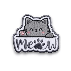 May include: Embroidered patch featuring a gray cat with pink accents, peeking over a white banner. The banner reads "Meow" with a paw print. The patch has a white border and is designed for application on fabric.