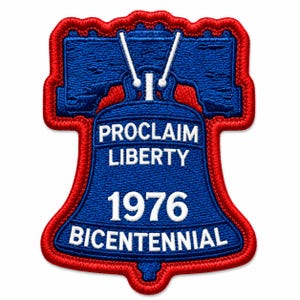 May include: An embroidered patch shaped like the Liberty Bell with a red border and a blue center. The text PROCLAIM LIBERTY is stitched in white above the year 1976 and the word BICENTENNIAL, also in white, on the bell's surface.