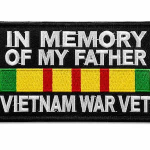 May include: A rectangular black embroidered patch featuring the white text IN MEMORY OF MY FATHER at the top and VIETNAM WAR VET at the bottom. Between the text is a horizontal ribbon with green, yellow, and red vertical stripes.