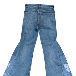 Op de afbeelding: Lichtblauwe jeans met een uitlopend pijpdesign. De jeans hebben een patchwork-ontwerp op de onderbenen met witte vlinder- en paisley-patronen. De jeans hebben twee achterzakken.