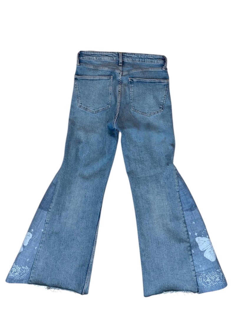 Op de afbeelding: Lichtblauwe jeans met een uitlopend pijpdesign. De jeans hebben een patchwork-ontwerp op de onderbenen met witte vlinder- en paisley-patronen. De jeans hebben twee achterzakken.
