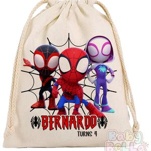 Puede incluir: Una bolsa beige con cord&oacute;n con tres personajes de dibujos animados de Spider-Man en rojo, negro y morado. La bolsa tiene un dise&ntilde;o de telara&ntilde;a negra y el nombre "Bernardo" con "Turns 4" impreso en rojo. El logotipo de Baby Bella est&aacute; en la esquina inferior derecha.