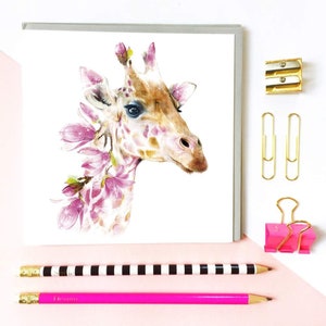 K&ouml;nnte beinhalten: Eine Aquarell-Illustration eines Giraffenkopfes, der von rosa Blumen umgeben ist. Die Giraffe hat ein hellbraunes Fell mit dunkelbraunen Flecken. Die Blumen sind hellrosa mit wei&szlig;en Zentren.