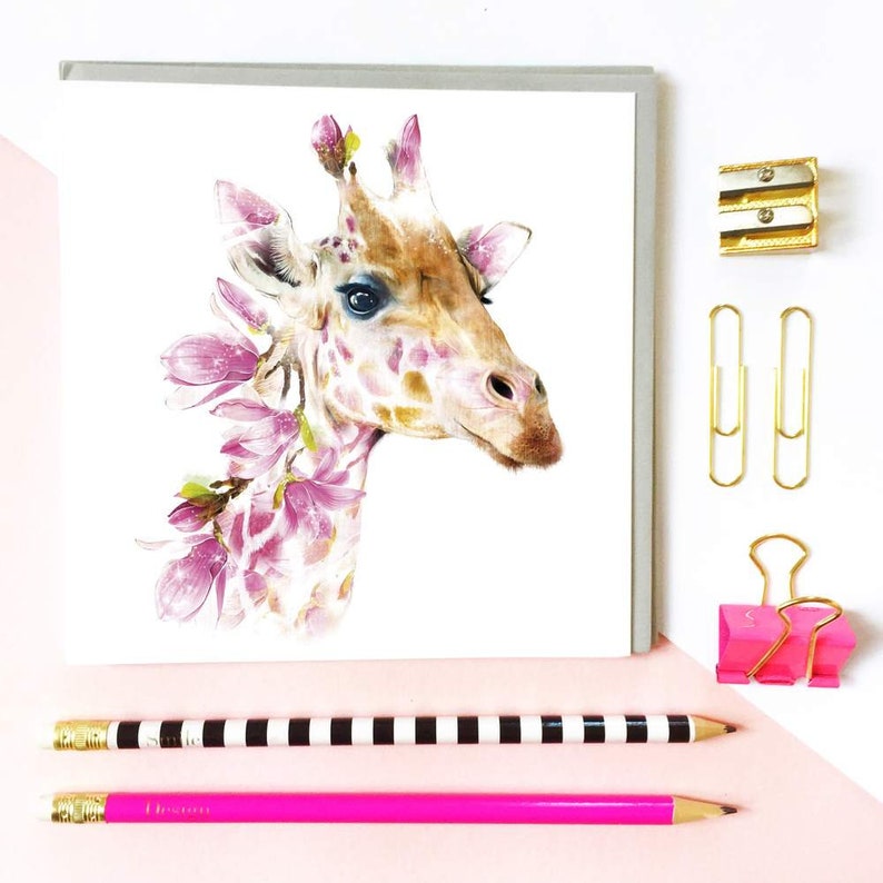 K&ouml;nnte beinhalten: Eine Aquarell-Illustration eines Giraffenkopfes, der von rosa Blumen umgeben ist. Die Giraffe hat ein hellbraunes Fell mit dunkelbraunen Flecken. Die Blumen sind hellrosa mit wei&szlig;en Zentren.