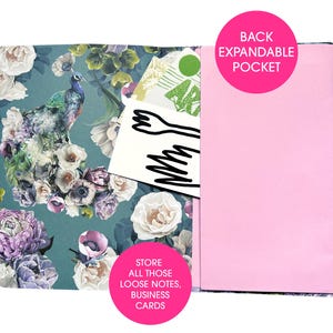 An open journal shows the inside back cover with a pink expandable pocket and a peacock and floral design on the left side.