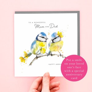 May include: A white card with a gray border features a watercolor illustration of two bluebirds perched on a branch with yellow flowers. The text "To a wonderful Mum and Dad" and "Happy Anniv" are printed on the card. The card also includes the text "Put a smile on your loved one's face with a special anniversary card."