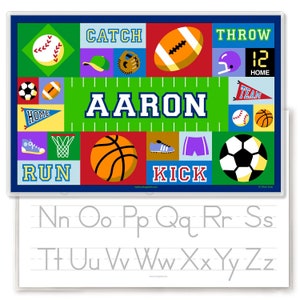 Sports place mat for kids. Child name in center on a green sports field in traditional letter men font, surrounded by colorful sports ball, and equipment.  Reverse side has alphabet letters for tracing.