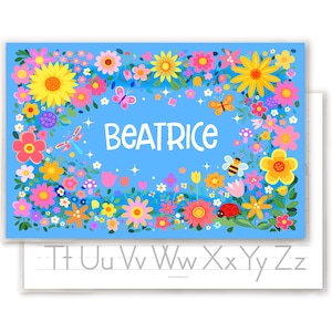 May include: A blue floral print with the name "BEATRICE" in white script. The design features colorful flowers, butterflies, and a bee. Below is a white sheet with the alphabet.