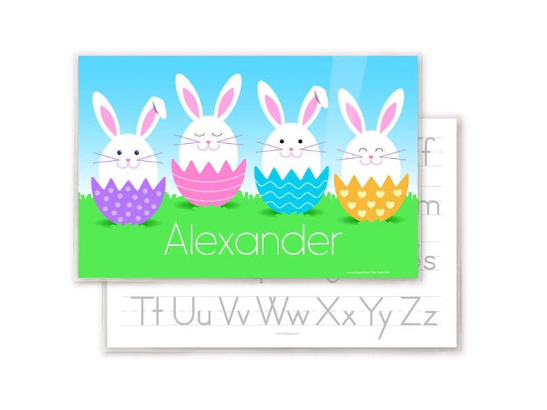 Easter Bunnies place mat for kids with 4 little bunnies, each sitting in a colorful Easter egg shell. Bunnies and eggs are on green grass with blue sky. Child's name is in white letters in grass.