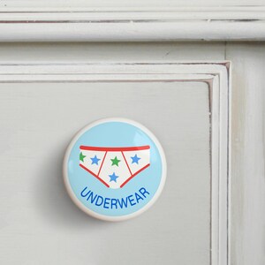 May include: A light blue round ceramic knob with a red, white, and green underwear design and the word "UNDERWEAR" printed below.