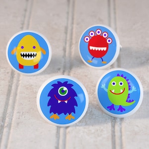 May include: Four ceramic knobs with different monster designs. The knobs are round and have a blue background. The monsters are yellow, red, blue, and green.