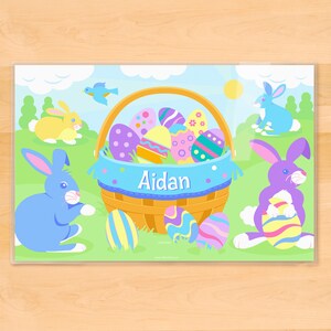 Easter place mat for kids with image of a Easter basket full of decorated eggs, with a blue liner.  Basket is in a spring scene with bunnies, flowers and butterfly and personalized with child name.