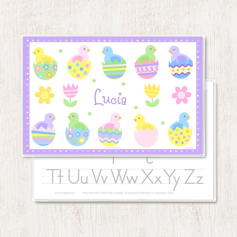 Easter place mat for kids has pastel chicks sitting in colorful Easter eggs shells with child name in the center of the mat.  Border of mat is pastel polka dots, name is in soft purple. Reverse side has alphabet letters.