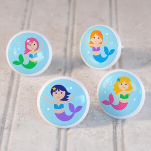May include: Four ceramic knobs with a blue background and a mermaid design. Each knob features a different mermaid with a different colored tail and hair. The mermaids are all smiling and have a star on their head.