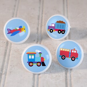 May include: Four ceramic knobs with blue backgrounds and colorful images of a red airplane, a blue dump truck, a blue train, and a red fire truck.