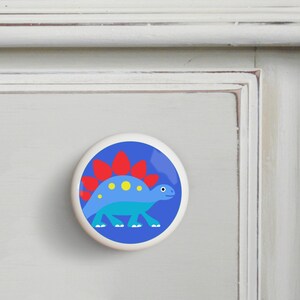May include: A blue and red dinosaur with yellow spots on a blue background. This is a ceramic knob for a drawer or cabinet.