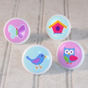 May include: Four ceramic knobs with colorful designs. The knobs feature a butterfly, a birdhouse, a bluebird, and an owl.