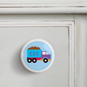 May include: A blue and purple toy dump truck with a brown load on a light blue background. The truck has three wheels and a red cab.