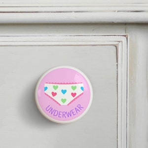 May include: Pink ceramic drawer knob with a white underwear design with colorful hearts and the word "UNDERWEAR" in purple text.