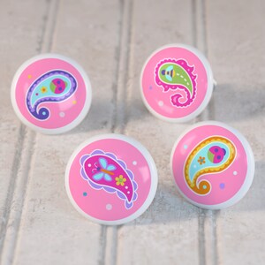 May include: Four pink ceramic knobs with a paisley design. Each knob features a different colorful insect, including a ladybug, a bee, a butterfly, and a dragonfly.