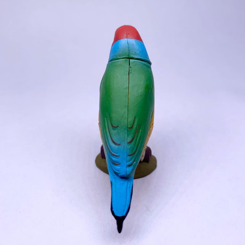 Puede incluir: Figurita de p&aacute;jaro colorida con cabeza roja, cuerpo azul y verde y cola azul. El p&aacute;jaro est&aacute; posado sobre una peque&ntilde;a base redonda marr&oacute;n. La figurita es de pl&aacute;stico y tiene un acabado brillante.