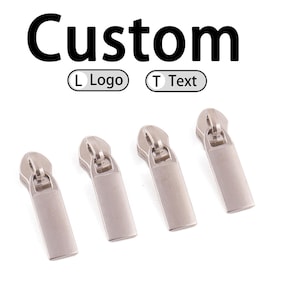 May include: Four silver-coloured zip pulls with rectangular tabs are shown against a white background. The word "Custom" is above the zip pulls, with options for "L Logo" and "T Text".