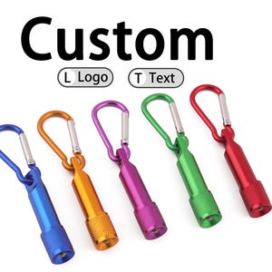 May include: A collection of five small, colorful flashlights with carabiner clips. The flashlights are blue, gold, purple, green, and red. The word "Custom" is displayed above the flashlights.