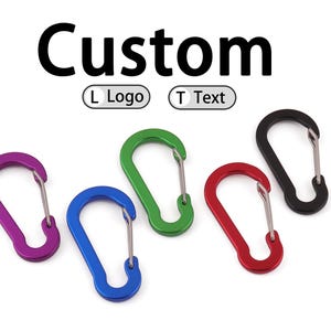 May include: A collection of colorful carabiner clips in purple, blue, green, red, and black. The word "Custom" is displayed above the clips, with options for "L Logo" and "T Text". These clips are ideal for attaching items.