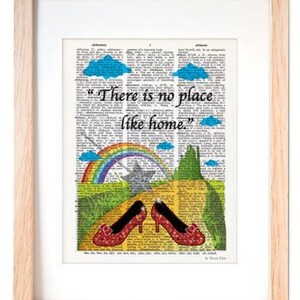 Puede incluir: Una impresión enmarcada de una página de libro vintage con un camino de ladrillos amarillos, un arcoíris y zapatillas de rubí. La cita "No hay lugar como el hogar" está impresa en la página.