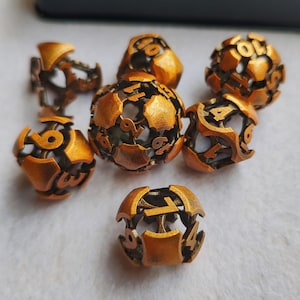 May include: A collection of seven bronze-colored, spherical dice. Each die features a cage-like design with visible numbers. The dice are arranged on a light-colored surface, showcasing their intricate, openwork construction. The numbers are clearly visible.