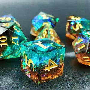 May include: Close-up of several polyhedral dice. The dice are made of clear resin with a mix of blue, green, and orange colors. The numbers are gold. The dice are for tabletop games.