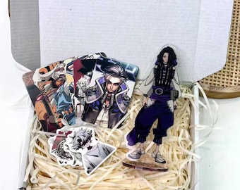 May include: A white box filled with decorative paper, containing several anime-style character cards and stickers. A clear acrylic figure of a character in purple pants and a white top stands in the box. The cards feature various characters.
